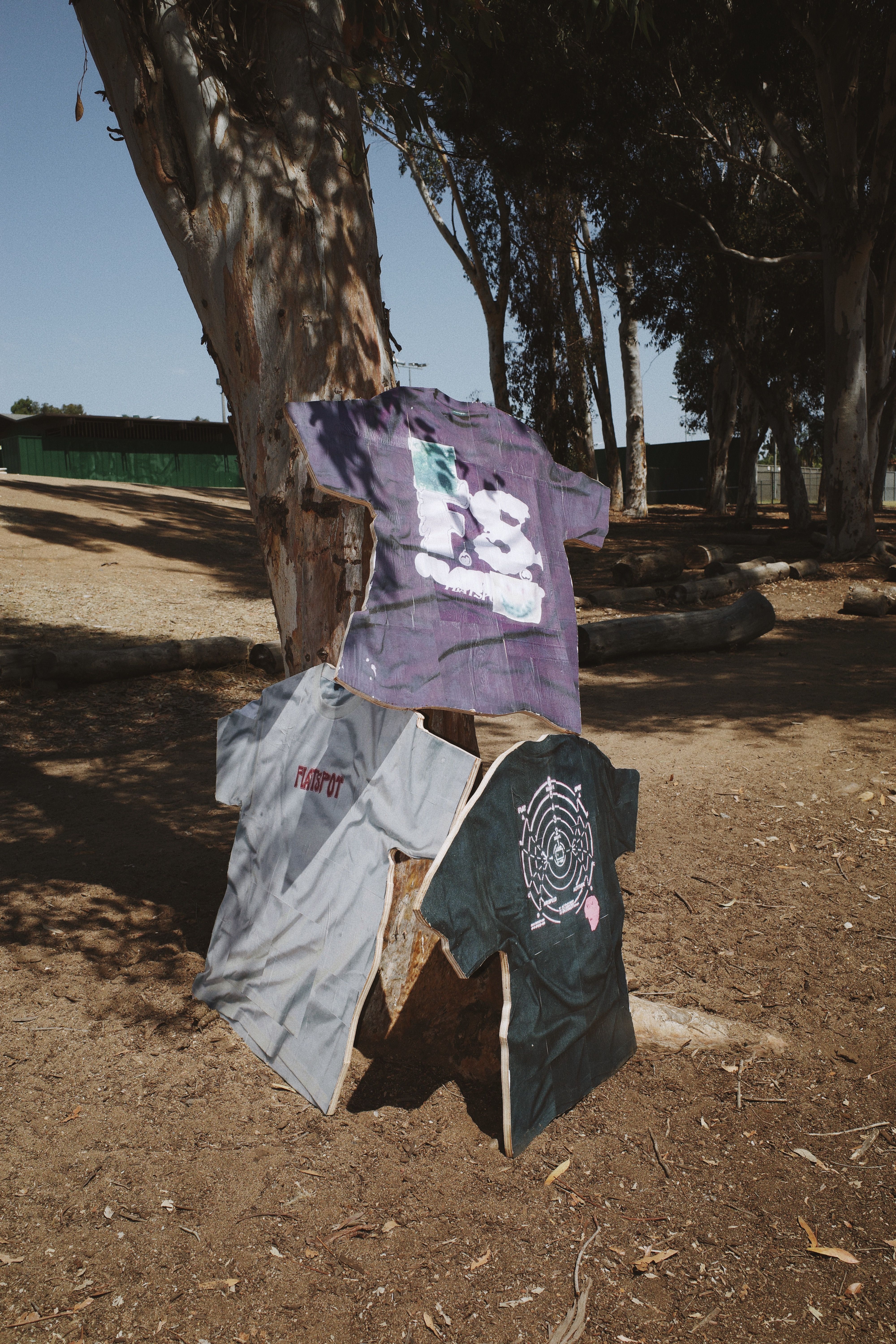 Flatspot AW21 Collection graphic tees printed onto wood cut-outs and stacked against a tree
